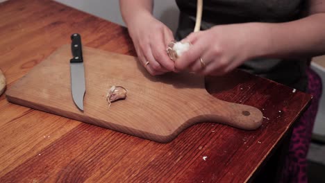 woman's hands are starting to peel garlic on a chopping board