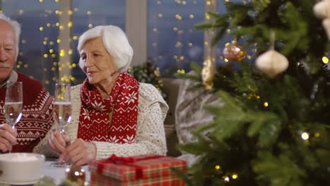 amorosa pareja de ancianos brindando con champán durante la víspera de año nuevo sentados a la mesa en casa