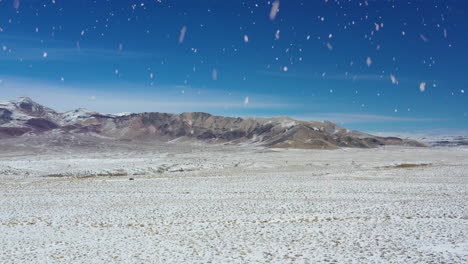 winter desert and mountain range during snowfall, aerial fly forward view