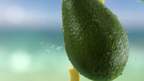 aguacate con rebanadas y salpicaduras cayendo en el fondo de la playa