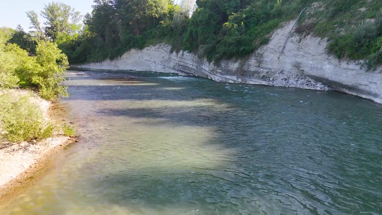 Inquadratura ampia statica di un fiume che scorre accanto a scogliere rocciose bianche sotto un cielo limpido e soleggiato