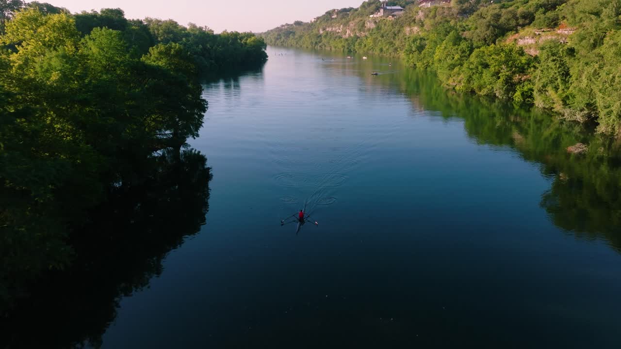 Kayaker paddling through glassy water during sunrise in Austin Texas, drone pull away to reveal downtown skyline from Redbud Isle nature trail