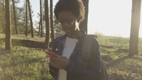 a pretty girl taking pictures of the forest at sunset with her cellphone