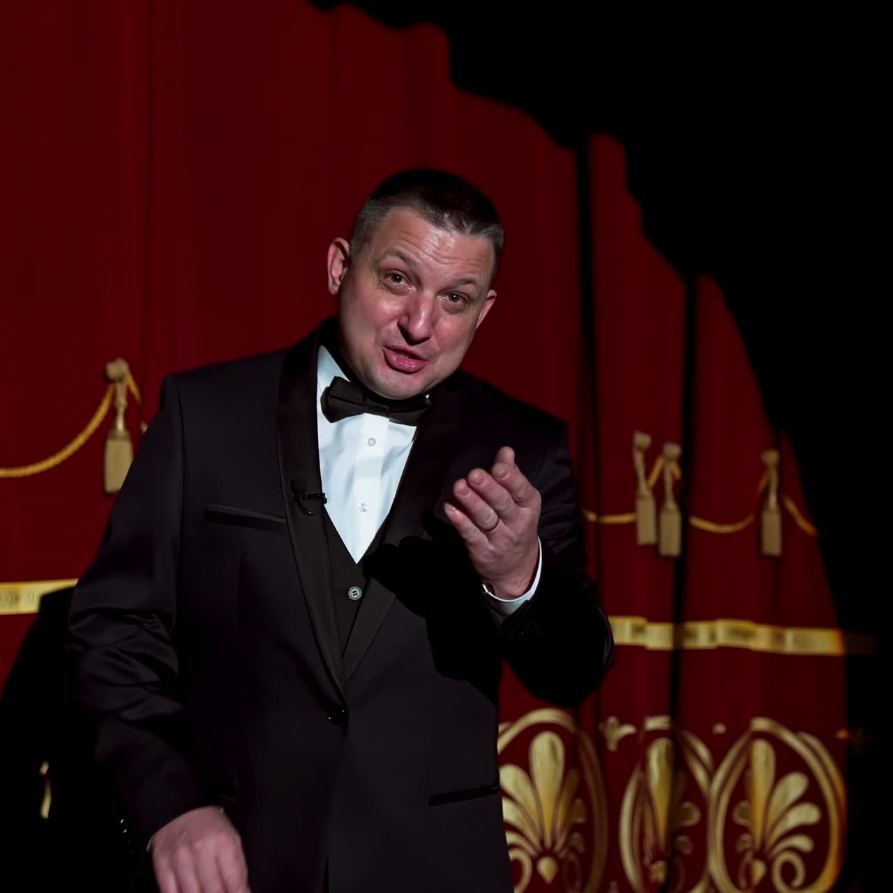 Announcer on a stage in theater. Bright round light on one person. Man in black suit performs to the auditorium