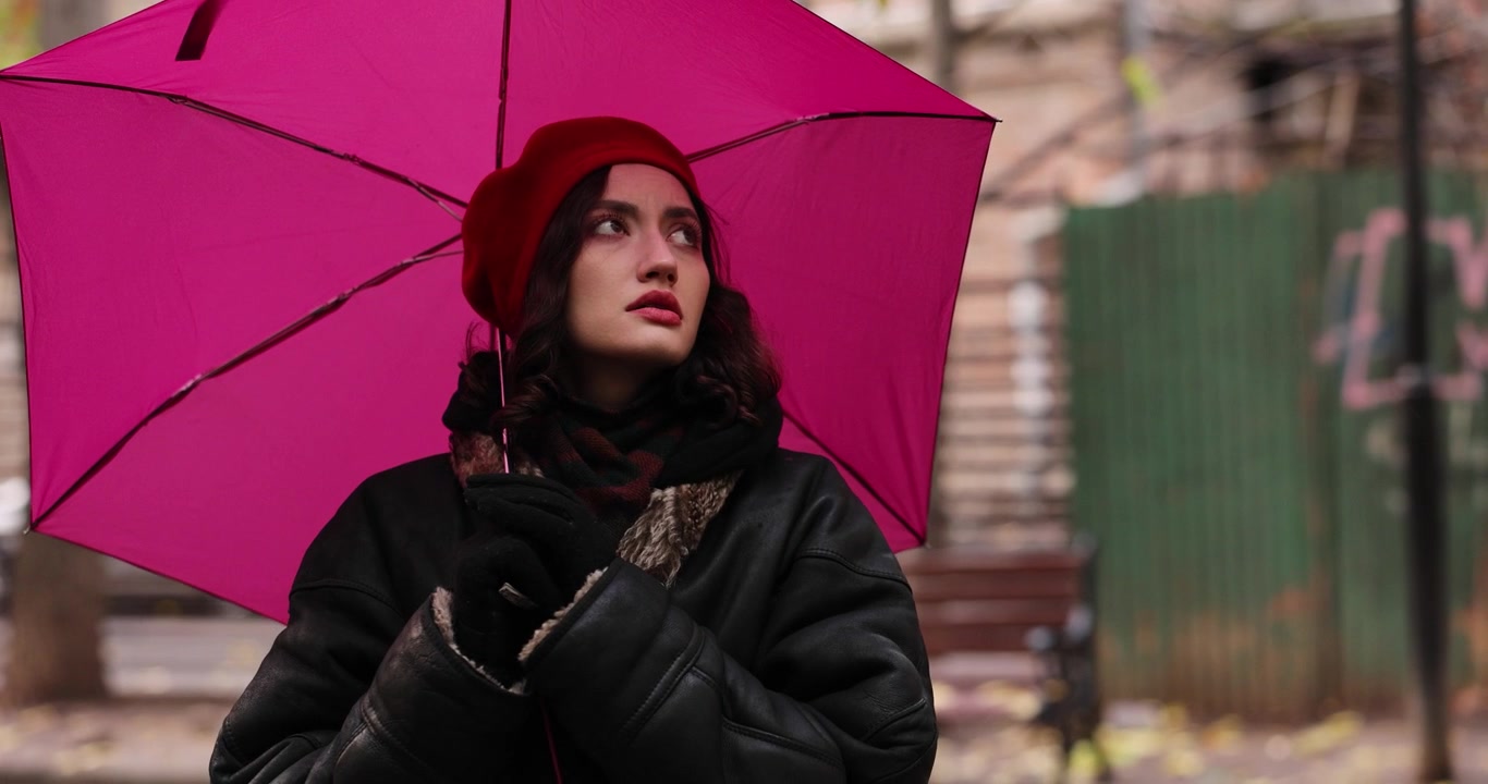 Donna elegante con basco rosso che tiene un ombrello rosa e guarda in alto