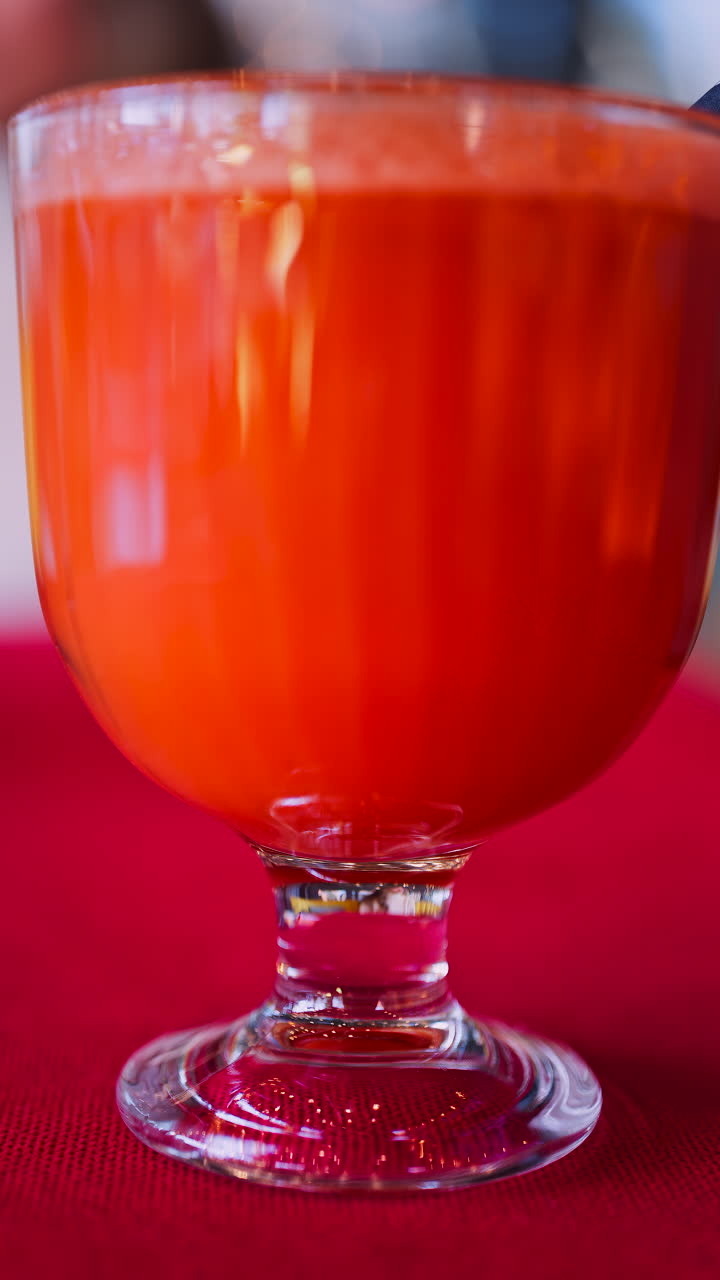 Primo piano di un succo di carota e arancia in un bicchiere con una cannuccia nera su una tovaglia rossa. Verticale