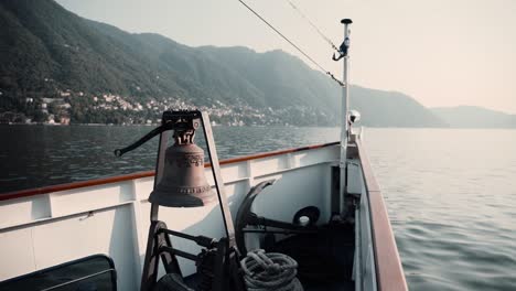 View-Of-A-Boat's-Bow-With-Bell-And-Anchor-Sailing-At-Lake-Como-In-Lombardy,-Italy---POV-shot