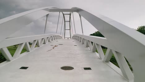 flying forward through a cycling bridge running across calm river moravia in slovakia revealing a person walking towards the camera. aerial sunset footage taken just before a storm
