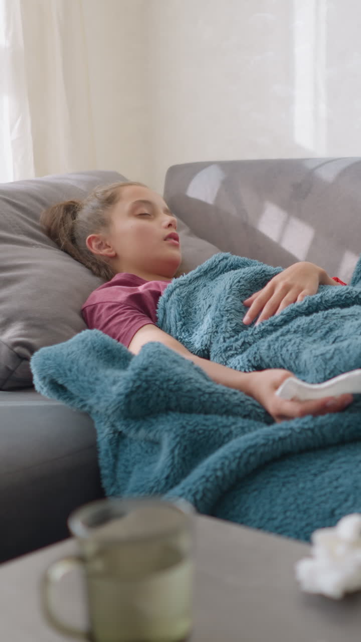 Bambina che dorme su un divano coperta da una coperta accogliente, con un’espressione serena e tranquilla, con della carta velina sparsa intorno e un bicchiere sul tavolo