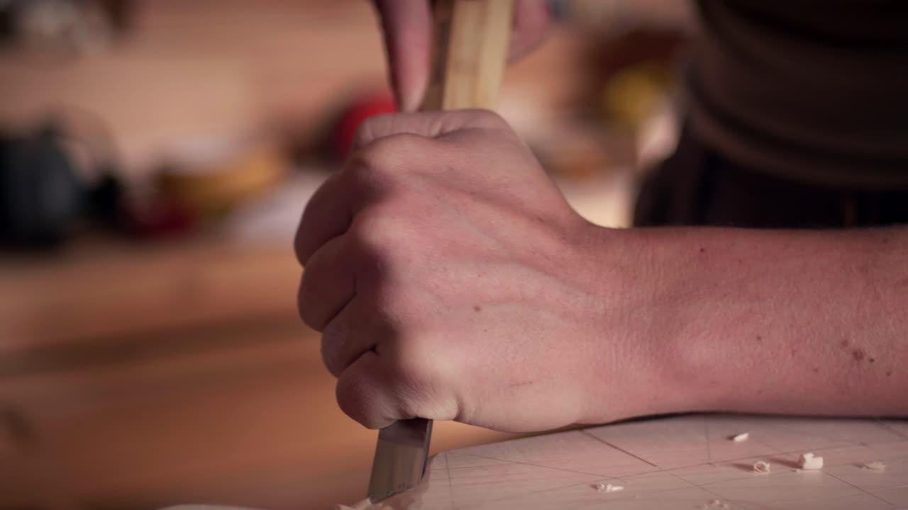 Hand-held chisel pressed into wooden surface by a professional artisan woodworker in a studio. Slow motion shot