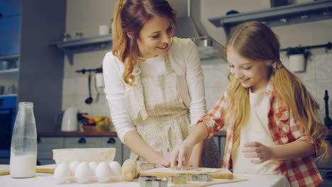 Small-pretty-girl-helping-her-mother-to-bake-cookies,-daughter-forming-a-daugh-and-showing-to-her-mom-in-the-kitchen.-Indoor