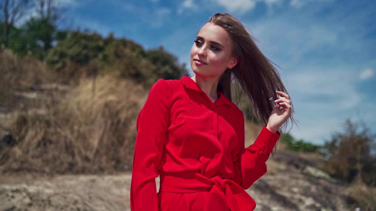 Portrait of attractive young woman. Gorgeous female in red dress standing among nature in summer with closed eyes.