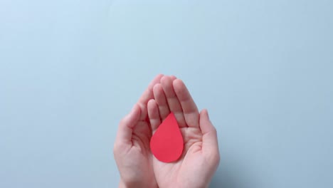 Hands-of-caucasian-woman-holding-blood-drop-on-blue-background-with-copy-space,-slow-motion