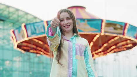 beautiful young caucasian girl showing thumbs up outside in a amusement park while wearing vibrating coulours