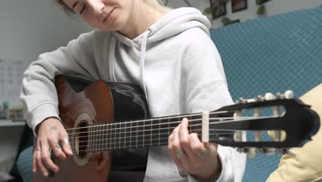young woman strumming an acoustic guitar in a cozy home environment