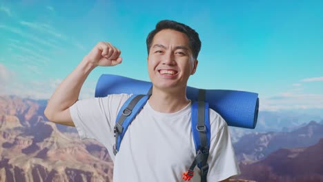 close up of asian male hiker with mountaineering backpack smiling and flexing his bicep while traveling at the top of mountain