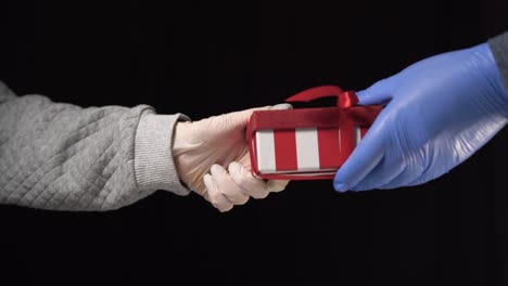 manos masculinas con guantes médicos dan dinero a cambio de una caja de regalos roja. concepto de compras de navidad durante la cuarentena