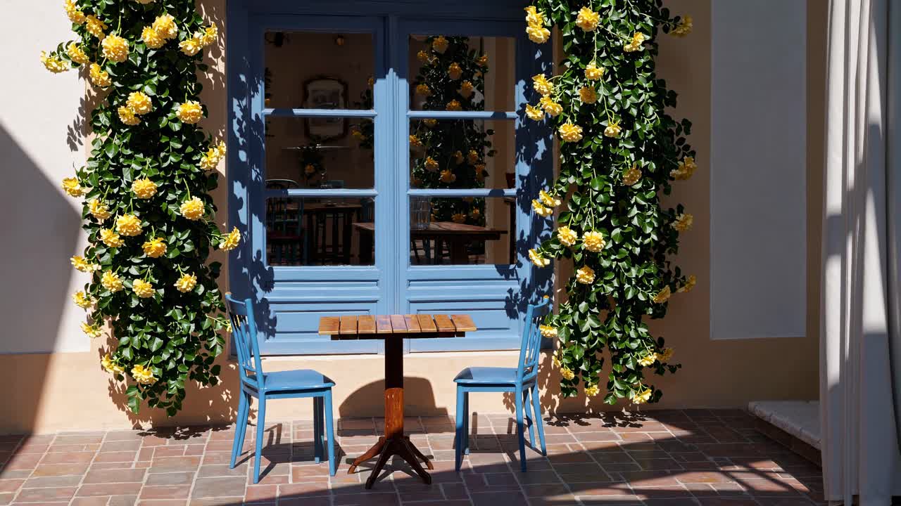 Charming cafe setting with blue chairs and table, framed by yellow flowers