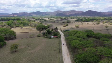 advancing grey vehicle on dirt road in costa rica near farmland, aerial dollyout shot