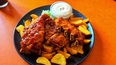 Closeup-served-dish-potato-wedges-with-beef-ribs-mayonnaise-tomato-sauce-dinning-orange-table-at-restaurant-with-cola-drink