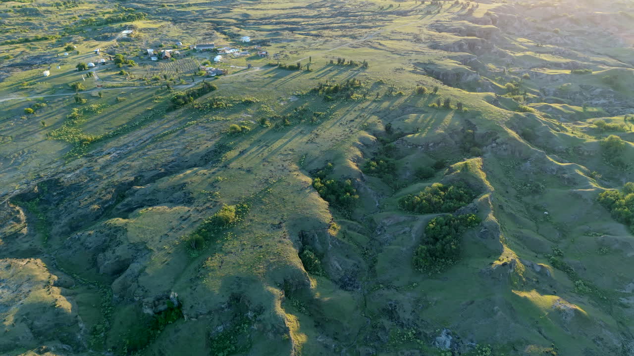 Drone video captures sweeping views over Tatacoa Desert's rugged terrain at sunset. Lit by golden hour light, shadows create dramatic contrasts on the textured landscape.