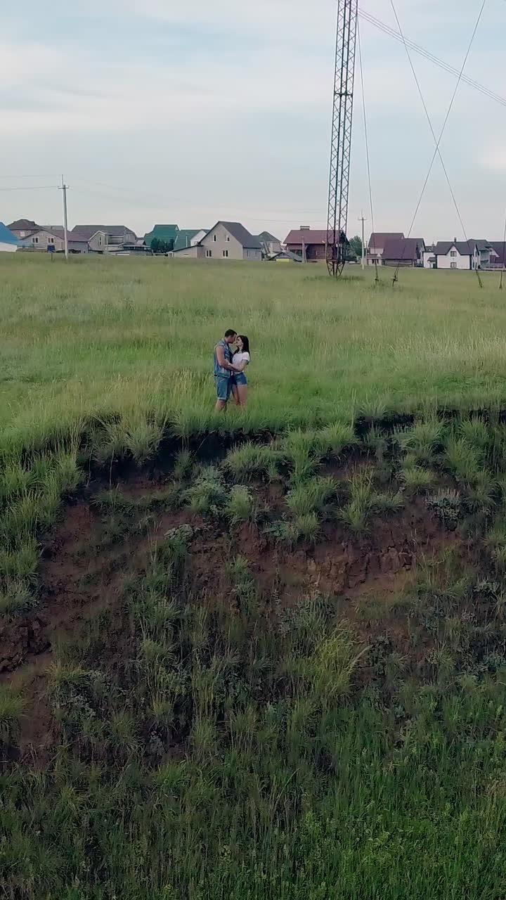 bird eye flight young couple hugs on green meadow edge against village building roofs in summer evening