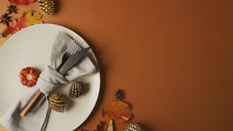 video of plate with cutlery and autumn decoration with leaves on orange surface