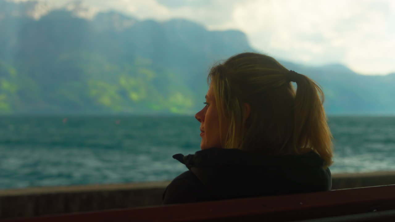 mujer sentada en un banco y mirando el mar en cámara lenta, mientras que los pétalos de la flor del cerezo vuelan en el viento