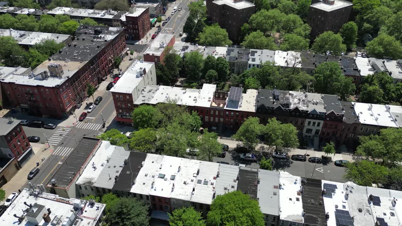 Aerial drone view of Brooklyn in spring, featuring lush green trees, classic brownstones, and quiet streets. Ideal for real estate, cityscape, and seasonal neighborhood imagery.
