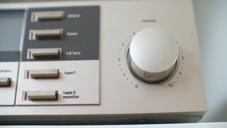 close up shot of adjusting the volume knob of an old vintage silver stereo system