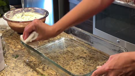 las manos femeninas engrasan el plato de cocina de vidrio preparándose para hacer la comida familiar en la cocina del hogar