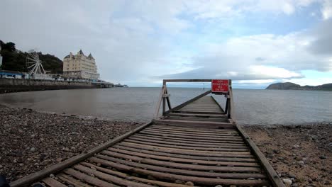 Time-lapse-waves-pulse-under-wooden-jetty-below-Llandudno-pier-overcast-seascape-dolly-left-slow