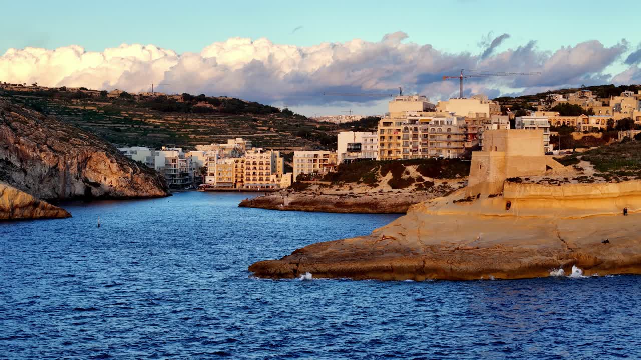Durante l'ora d'oro, la storica Torre Xlendi del XVII secolo si erge imponente su un promontorio calcareo, affacciata sulle acque blu intenso del Mediterraneo e sull'incantevole villaggio costiero di Xlendi, Gozo.