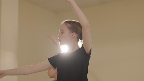 a group of young ballet students in black dancewear practicing positions in a spacious ballet studio with wooden flooring and wall-mounted barres. focused expressions and synchronized movements.