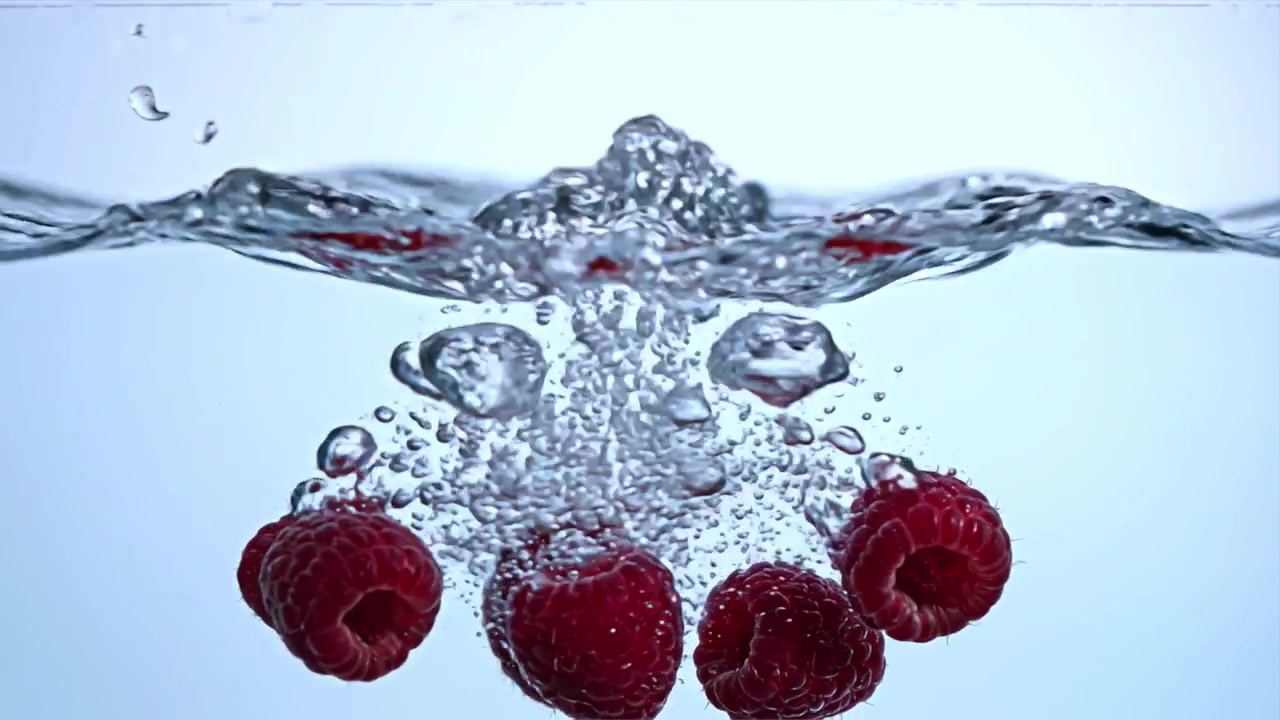 Fresh Red Raspberries Splashing into Clear Water