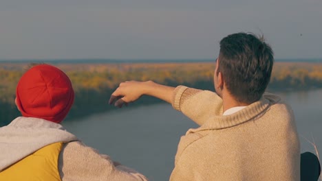 guy throws rock into calm river water sitting near friend