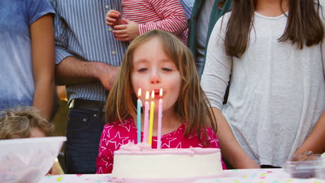 young girl blowing out candles at her birthday garden party