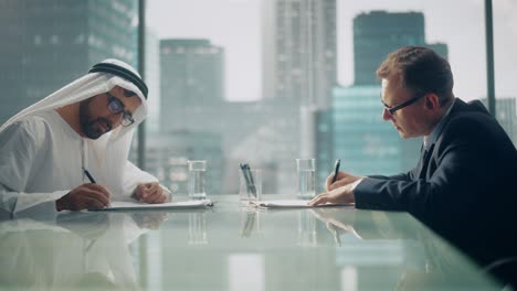 dos hombres de negocios multiculturales exitosos sentados en el cargo y firmando un contrato. un socio de negocios árabe estrecha la mano con un inversor en un lucrativo acuerdo financiero. saudi, emirati, concepto de hombre de negocios árabe.