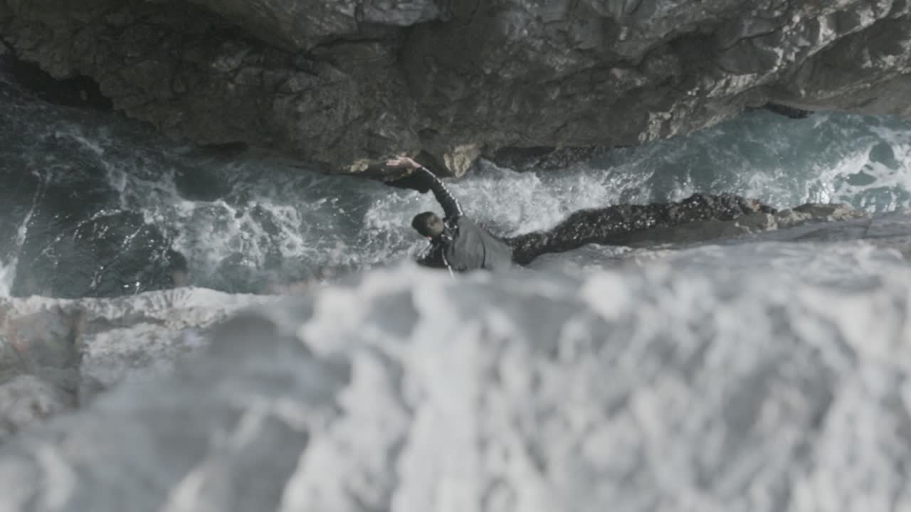 hombre trepando por la costa rocosa cerca de las olas del océano