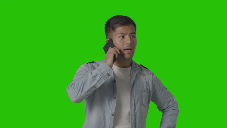 Studio-Shot-Of-Casually-Dressed-Serious-Young-Man-Talking-On-Mobile-Phone-Against-Green-Screen-