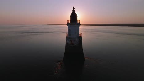 abandoned lighthouse in very calm tidal waters with rise revealing setting sun over top of structure. plover scar lighthouse, lancashire, uk.