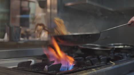 shot inside a kitchen of an italian restaurant where a cook prepares pasta in a pan