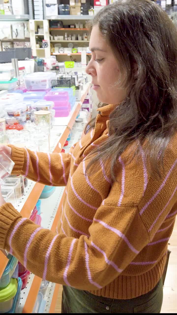 Young woman choosing small glass containers in a large store.