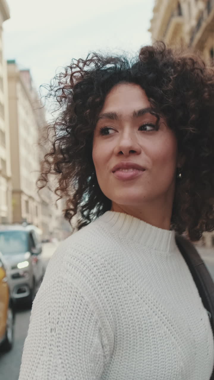 Mulher de cabelo cacheado usando um suéter em uma rua da cidade