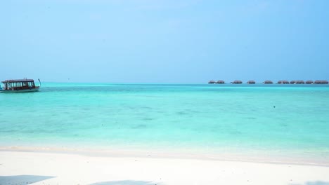 Maldives-boat-moving-across-tropical-blue-water-toward-overwater-bungalows