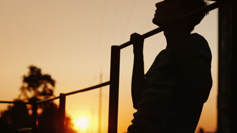 teenage boy pulls himself up on a horizontal bar in the yard street training and sports among youth