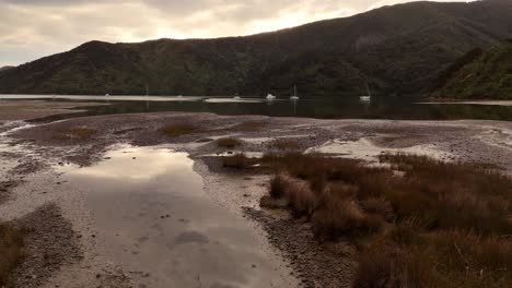 estuary during low tide at sunset, sailboats anchored in bay, marlborough sounds, south island, new zealand. aerial backward at low altitude