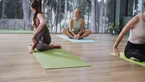 focused diverse women stretching together on mats in yoga class with female coach, slow motion