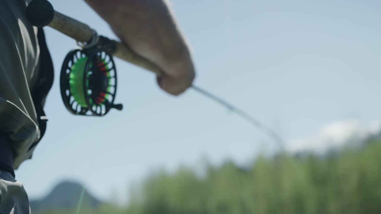 Bir adam sinek avı yapıyor ve misinasını geri sarıyor.