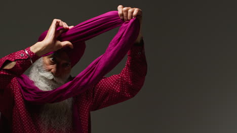 fotografía de iluminación de estudio de baja clave de un hombre sikh anciano con barba atando tela para turbante contra un fondo oscuro mirando en el espejo 1